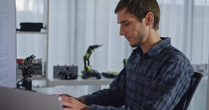 Young adult male freelance developer typing write prompt AI bot app program nomad terminal with coding at office. Artificial intelligence dashboard, robotics, user interface, machine learning concept.