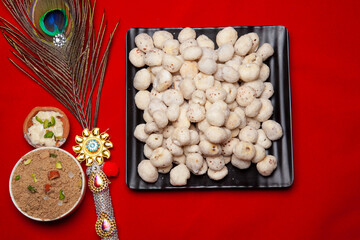 Traditional Prasad Makhana Offering with Decorative Peacock Feather on Red Background