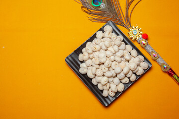 Traditional Prasad Makhana Offering with Decorative Peacock Feather on Yellow Background