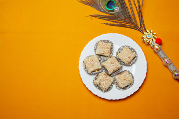 Traditional Festival Barfi Dessert on a white Plate with a Decorative Peacock Feather and a Yellow Background