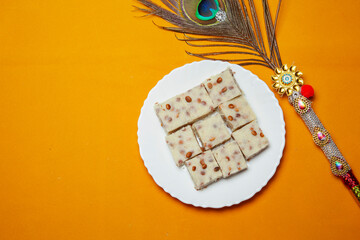 Traditional Festival Barfi Dessert on a white Plate with a Decorative Peacock Feather and a Yellow Background