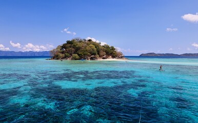 Tropical island with clear turquoise waters and paddleboarder.