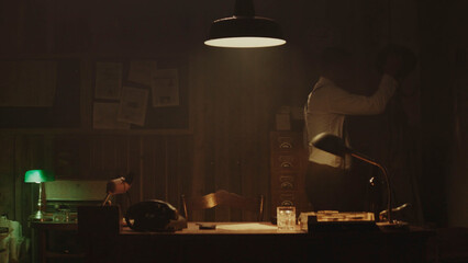 Detective pinning evidence on wall in dark office at night