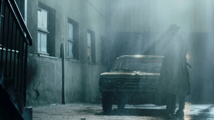 Mysterious man walking in rain near vintage car at night