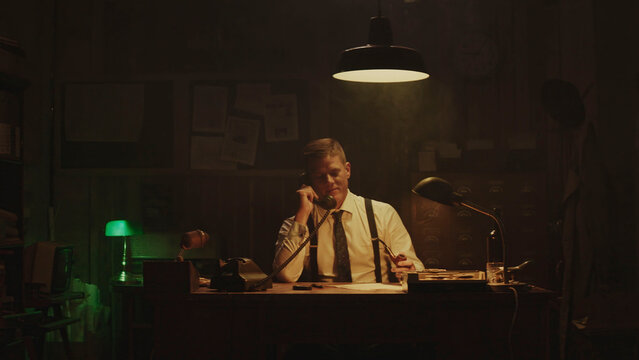 Focused detective working late at night in his office, taking notes while on the phone - Powered by Adobe