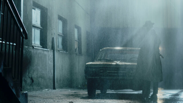 Mysterious man walking in rain near vintage car at night