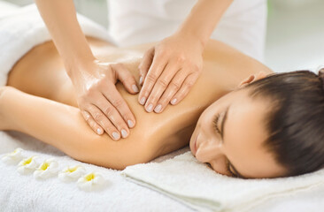 Beautiful young woman receiving relaxing shoulder massage from masseur in luxury spa center. Close up of relaxed client enjoying wellness therapy and body stress relief during relaxing spa procedure.