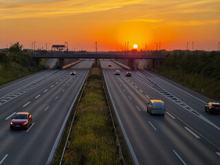 Obraz premium Soft golden light falls over a Danish highway at sunset, illuminating the moving cars and creating a calm, cinematic scene with warm skies and smooth perspective.