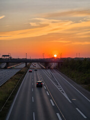 Warm sunset over a highway with light traffic and soft clouds on the horizon. Peaceful evening scene with cars driving toward the fading daylight.