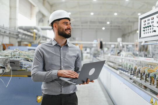 Smiling engineer using laptop supervising production line in factory