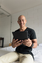 Bald Hispanic man sitting on bed at home using digital tablet computer © Ranta Images