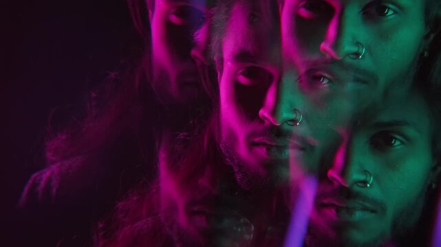 Close up portrait of handsome Indian man with long hair and piercing posing for camera on black background in purple neon lighting, kaleidoscope cloning effect