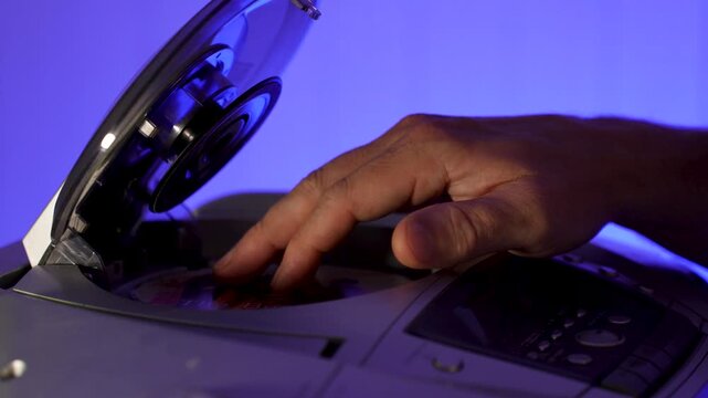 A close-up of a hand inserting a compact disc CD into the open tray of an old or vintage portable CD player