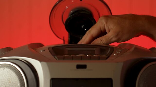 A close-up of a hand inserting a compact disc CD into the open tray of an old or vintage portable CD player