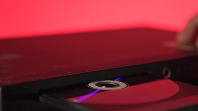 A close-up of a hand inserting a compact disc CD into the open tray of an old or vintage portable CD player