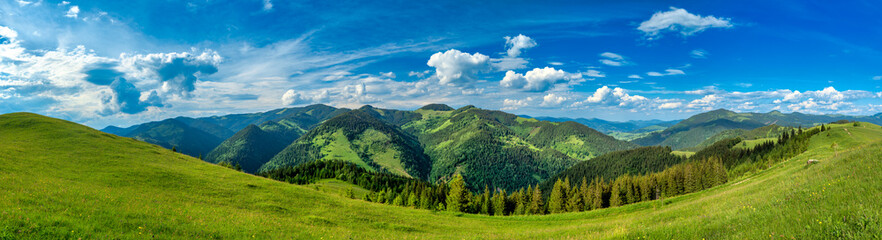 Wide angle panoramic landscape of Carpathian Mountains with green hills, scenic forests and clear blue summer sky