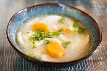 Broth with dumplings, carrots and parsley in a decorative bowl.
