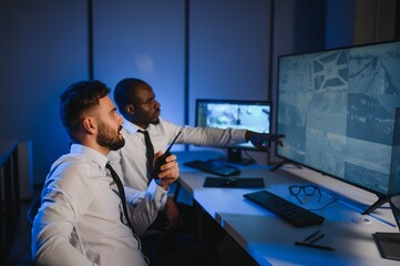 Two security guards sitting by workplace in front of monitors and observing cctv video
