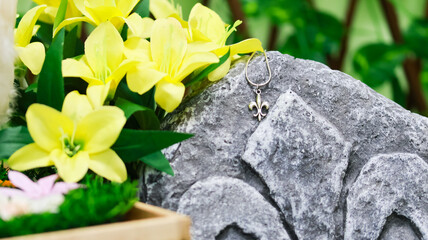 Close-up of a silver fleur-de-lis pendant displayed on a stone relief with carved lily symbol,...