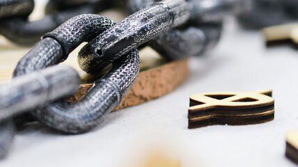 Macro close-up of a heavy metal chain placed on a surface with scattered wooden symbol pieces. The...