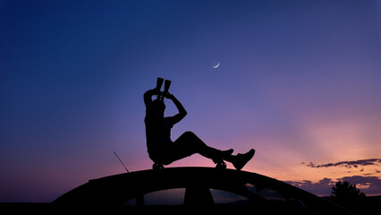 Man watching stars, Milky Way, planets, Moon and other celestial objects from a car rooftop from a...