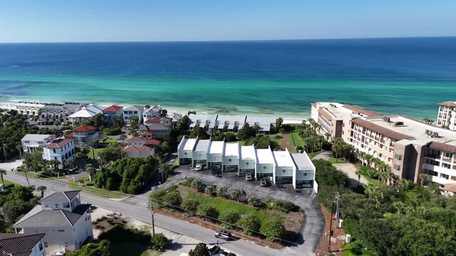 Aerial fly over the coastal settlement with apartments and turquoise ocean along white sandy beach, 30A, Florida, USA