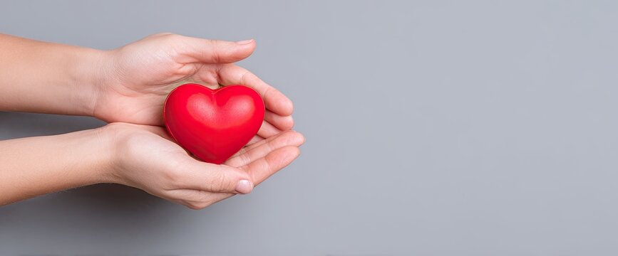 Hands holding a red heart against a gray background