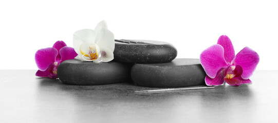 Acupuncture needles, orchid flowers and spa stones on grey textured table against white background, closeup