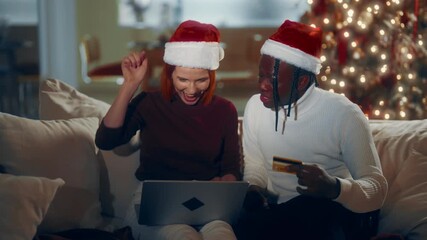 Cheerful customers of web-store ordering gifts online in Christmas holidays. Happy black man and his beloved caucasian lady shopping online and celebrating winter holidays, laughing multiethnic people