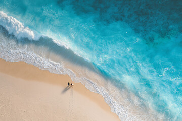 Aerial view of two people walking along a pristine sandy beach with turquoise waves gently crashing ashore