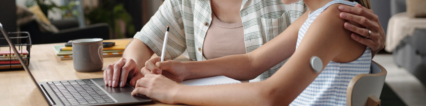 Mother helping daughter check glucose on laptop at home