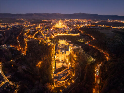 Aerial view of the Alc&Atilde;&iexcl;zar of Segovia perched majestically on a rocky crag, glowing warmly against the cool twilight, Segovia Cathedral stands tall in the cityscape, Segovia, Castilla y Le&Atilde;&sup3;n, Spain.