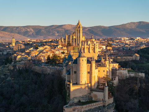 Aerial view of the Alc&Atilde;&iexcl;zar of Segovia bathed in golden sunlight, its medieval architecture contrasting with the distant, hazy mountains, Segovia, Castilla y Le&Atilde;&sup3;n, Spain.
