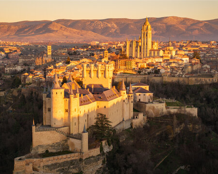 Aerial view of the Alc&Atilde;&iexcl;zar of Segovia basks in the golden light of dawn, contrasting with the distant, shadowed mountains and the city's cathedral, Segovia, Castilla y Le&Atilde;&sup3;n, Spain.