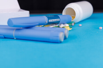 Healthcare image with semaglutide injection pens, white pill bottle and scattered pills on a blue table background.