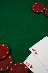 A green felt poker table is set up with red gaming chips scattered around. Two aces of hearts and diamonds are face up, suggesting a potential winning hand during an intense game.
