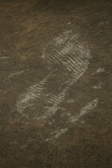 A clear dusty footprint on a dark, dirty floor surface, showing shoe tread pattern and suggesting movement, activity, or an abandoned space.