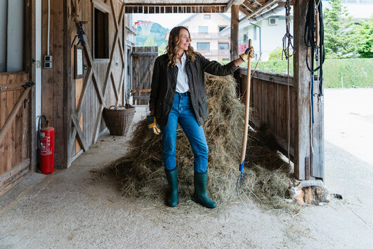 Woman in stable with pitchfork near haystack promoting agritourism