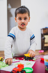 Child playing with kinetic sand and toy trucks wearing fake mustache