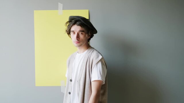 Medium slowmo portrait of stylish young Caucasian man in beret posing for camera on ultimate gray background