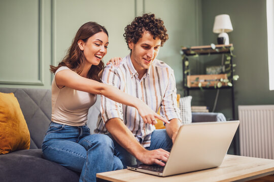 Adult couple is sitting at sofa at home and using laptop. They are shopping online and searching for goods.