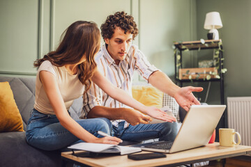 Couple discussing home finance on laptop and calculating family budget in living room. They are distraught.