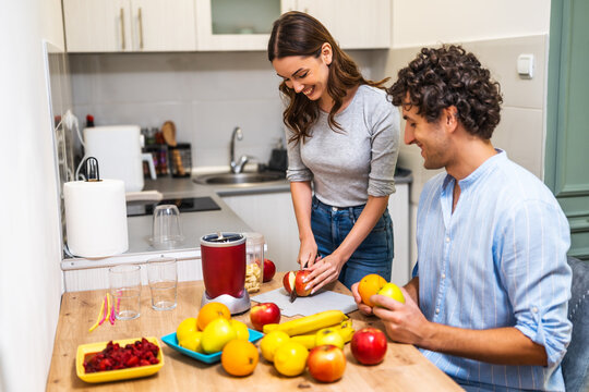 Adult couple is preparing smoothie in their kitchen. They have various fruits ready to be mixed in electric juicer. - Powered by Adobe