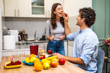Adult couple is preparing smoothie in their kitchen. They have various fruits ready to be mixed in electric juicer.
