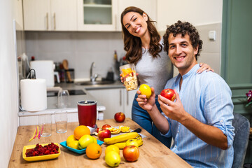 Adult couple is preparing smoothie in their kitchen. They have various fruits ready to be mixed in electric juicer.