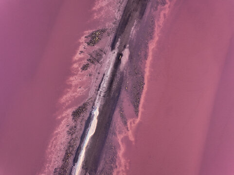 Aerial view of a striking contrast between the vibrant pink waters and the stark, linear land formation, Aigues-Mortes, Occitanie, France.