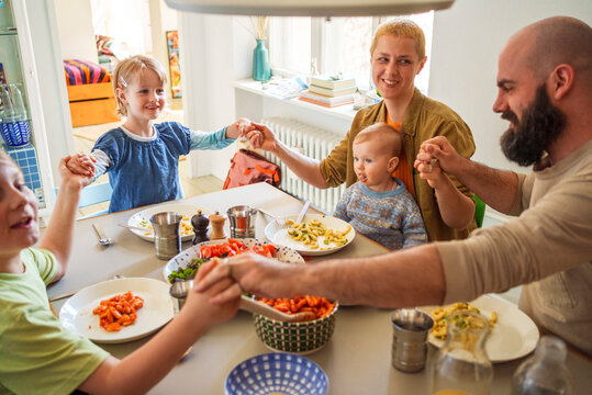 Family holding hands sitting at dining table