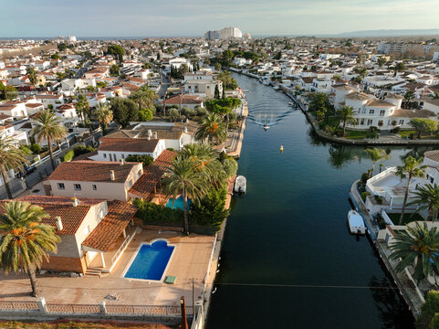 Empuriabrava, Spain - 31 December 2023: Aerial view of canals cutting through the town, reflecting the clear blue sky, surrounded by terracotta rooftops and lush green gardens.