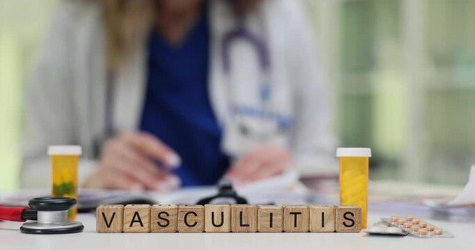 Doctor takes notes at desk with Vasculitis on blocks and medication bottles on table. Condition involves inflammation of blood vessels slow motion