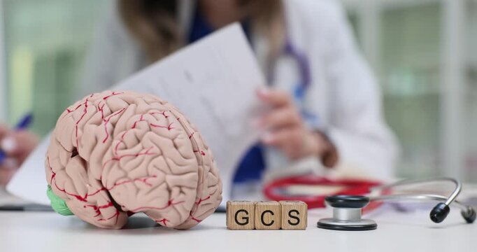 Lady doctor reviews prescription near GCS on blocks and model of brain. Glasgow coma scale suggests discussion diagnosis and assessment at appointment